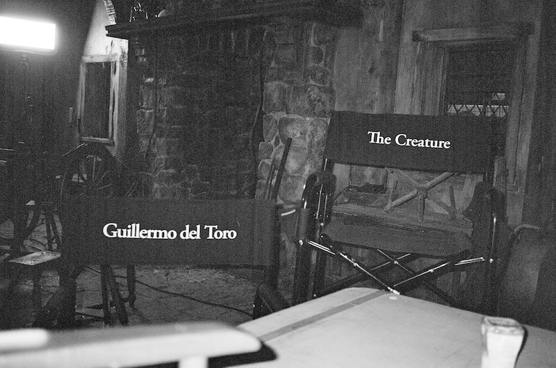 A black-and-white image of two chairs on the set of Frankenstein, one that says Guillermo del Toro and one that says the Creature.