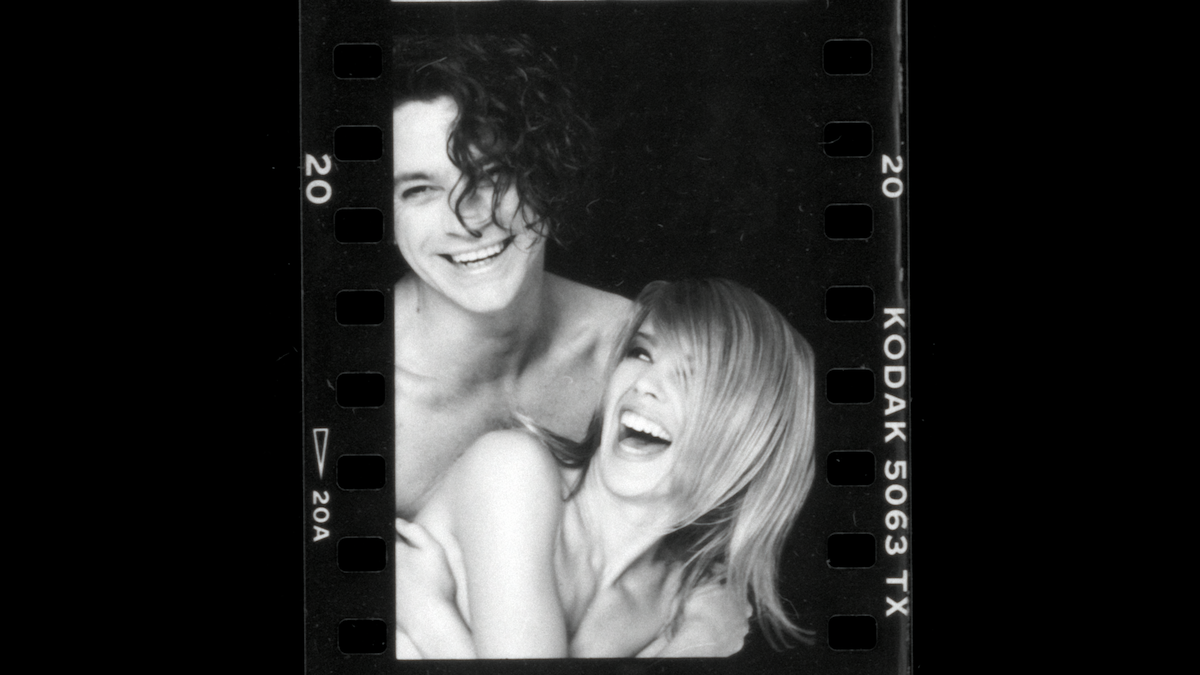 Black and white photo of a smiling man and woman posing closely, both laughing, against a simple studio background, with visible film strip edges labeled "Kodak 5063 TX".
