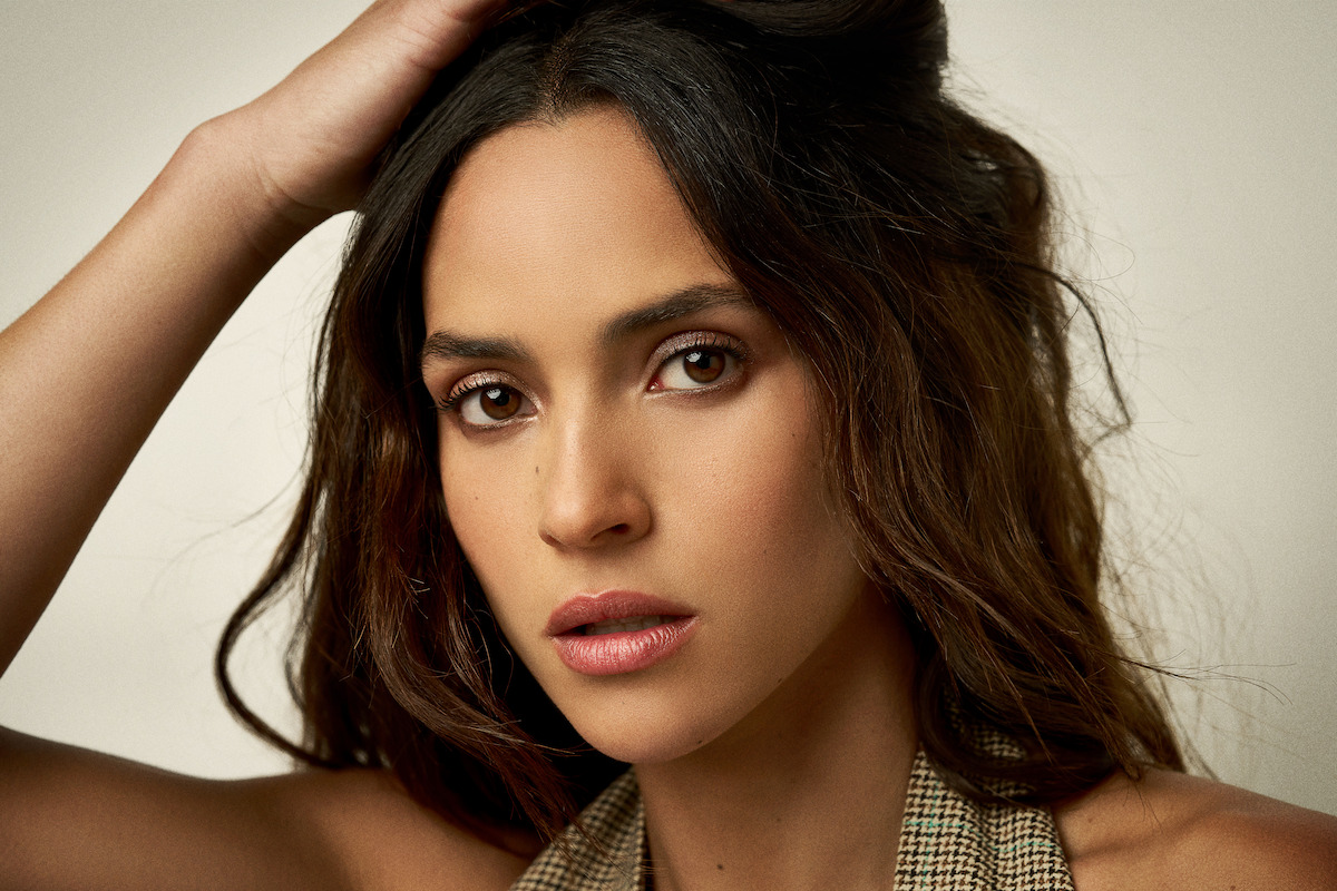 Adria Arjona wears a vest and runs her hand through her hair.