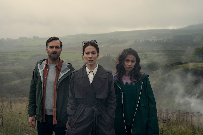 Will Forte as Gilbert Power, Siobhán Cullen as Dove, and Robyn Cara as Emmy Sizergh stand on the Irish countryside together in 'Bodkin'
