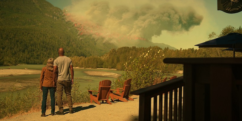 Annette O’Toole as Hope and Colin Lawrence as Preacher stand watching a wildfire blaze through a mountainside in Season 5 of ‘Virgin River.’