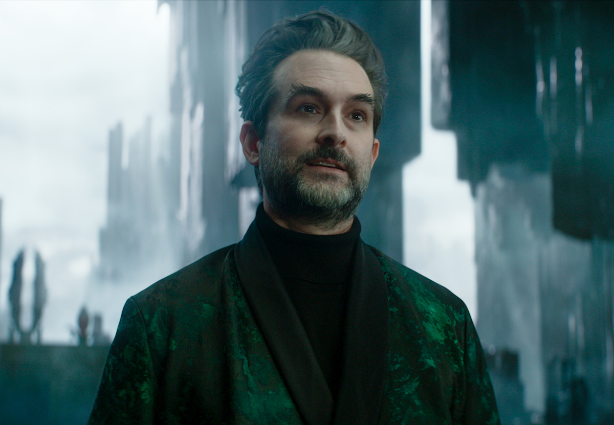 Homem de cabelos e barba grisalha veste um sobretudo verde em representação do inferno na série ‘Percy Jackson’