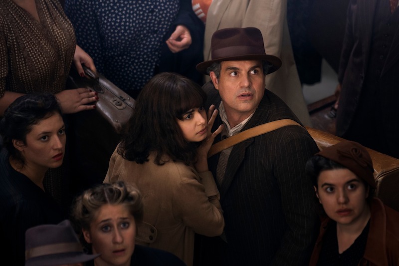 (L to R) Aria Mia Loberti as Marie-Laure, Mark Ruffalo as Daniel LeBlanc  - they are standing in a crowd, while looking up in shock at something offscreen. 