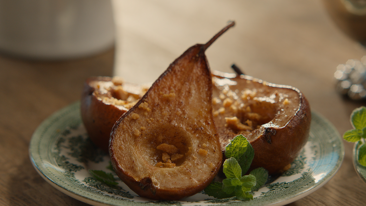 Baked pear halves with crumb topping on a decorative plate, garnished with fresh mint leaves. Warm, cozy table setting with soft natural light, evoking a comforting and inviting mood.