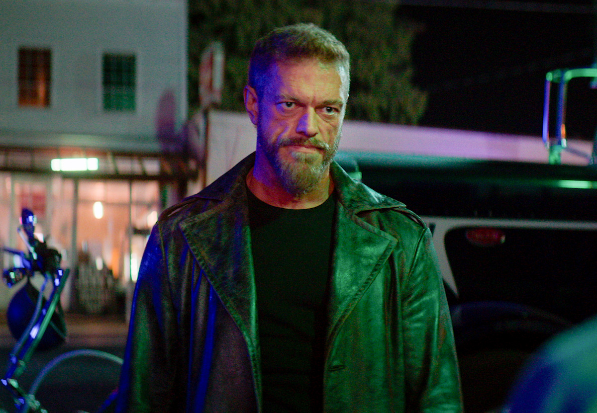 Homem de cabelos e barba grisalha veste um sobretudo verde na série ‘Percy Jackson’