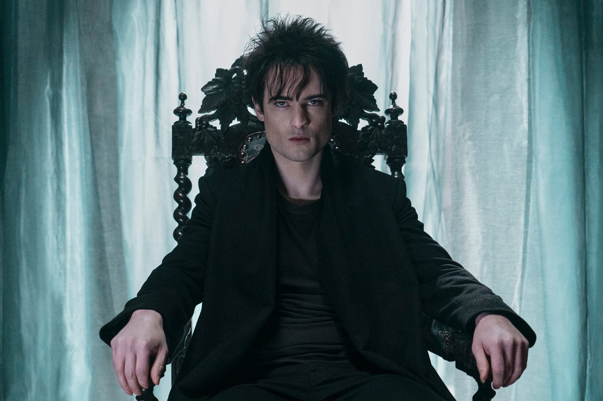  A man with tousled hair sits in a wooden chair