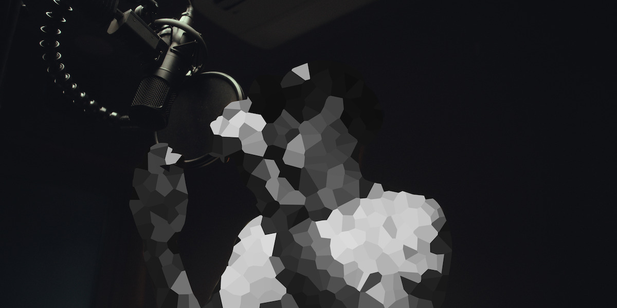 Person recording vocals in a dimly lit studio, standing in front of a microphone, image is pixelated for privacy.