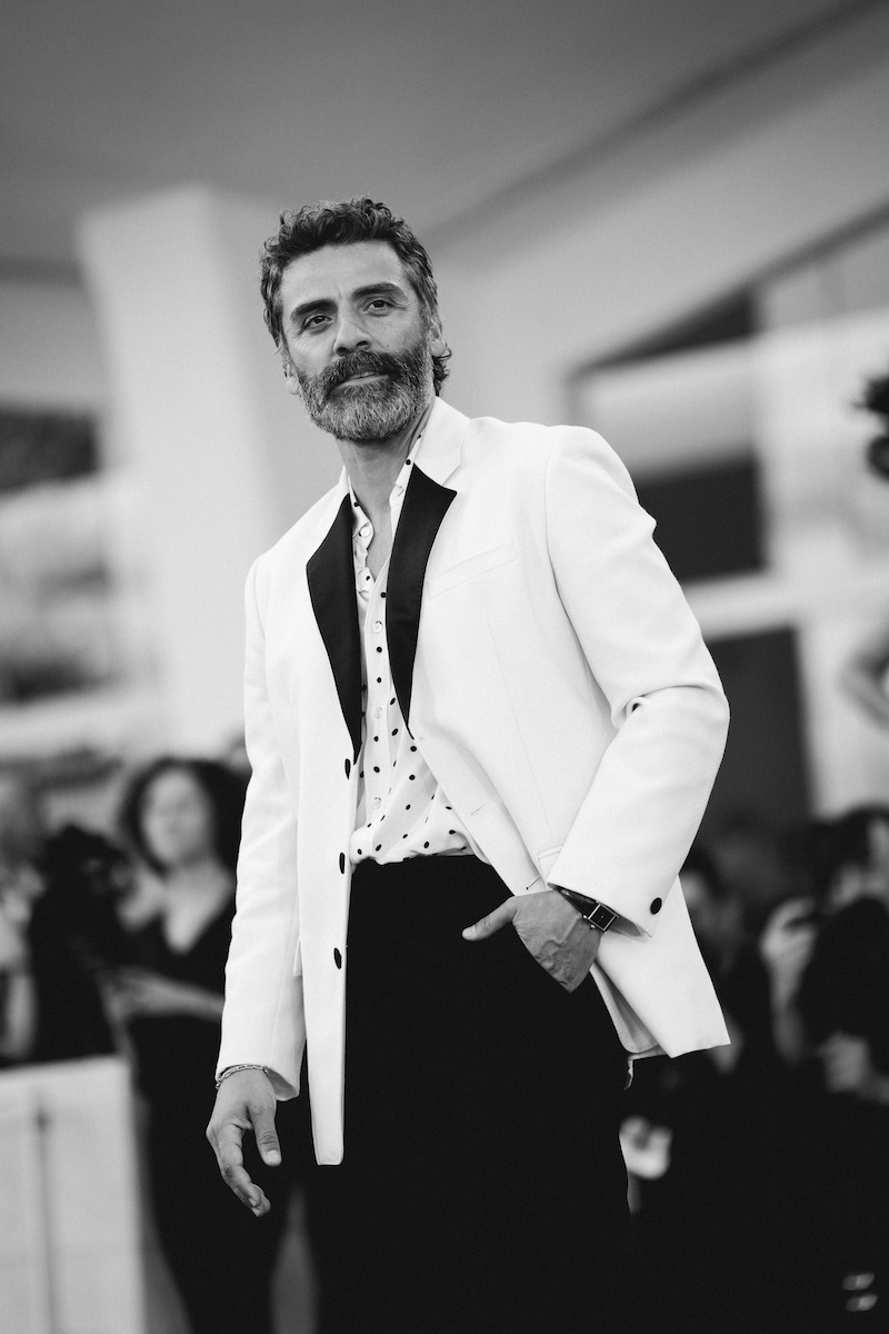Oscar Isaac in a white tuxedo jacket and polka dot shirt on the red carpet.