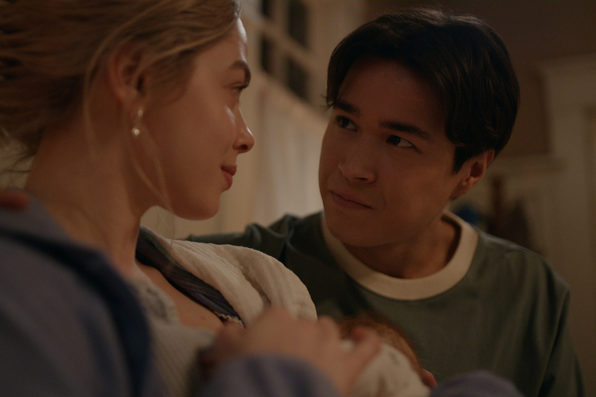 A young couple holds a newborn baby in a warm, softly lit indoor setting, gazing at each other lovingly, suggesting a tender family moment at home.