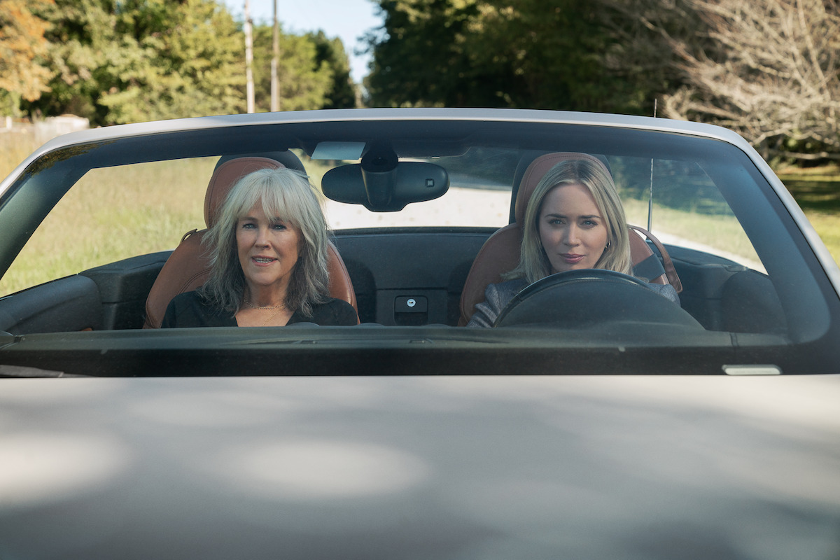 A silver-haired Catherine O’Hara sits in the passenger seat of a white convertible as Emily Blunt drives in ‘Pain Hustlers.’