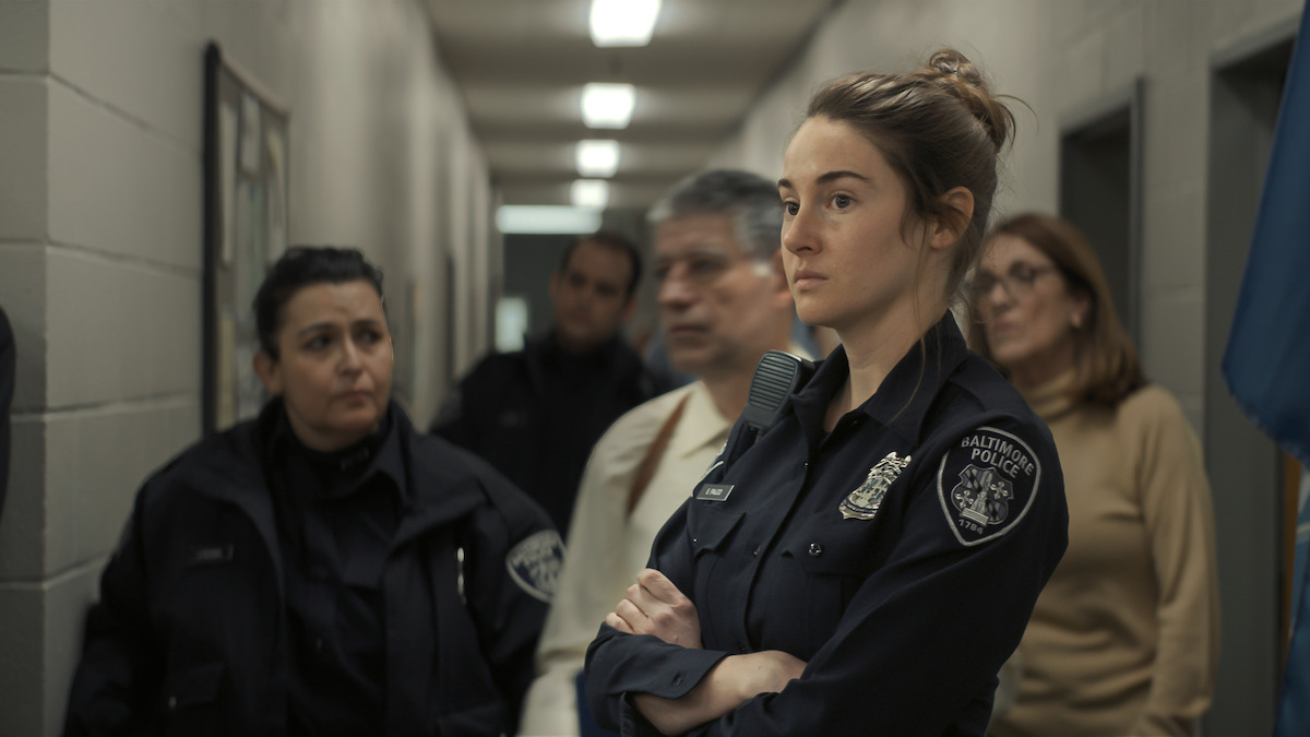 Shailene Woodley wears a police uniform while standing in a hallway with a few unknown people behind her in a still image from the film ‘To Catch a Killer.’
