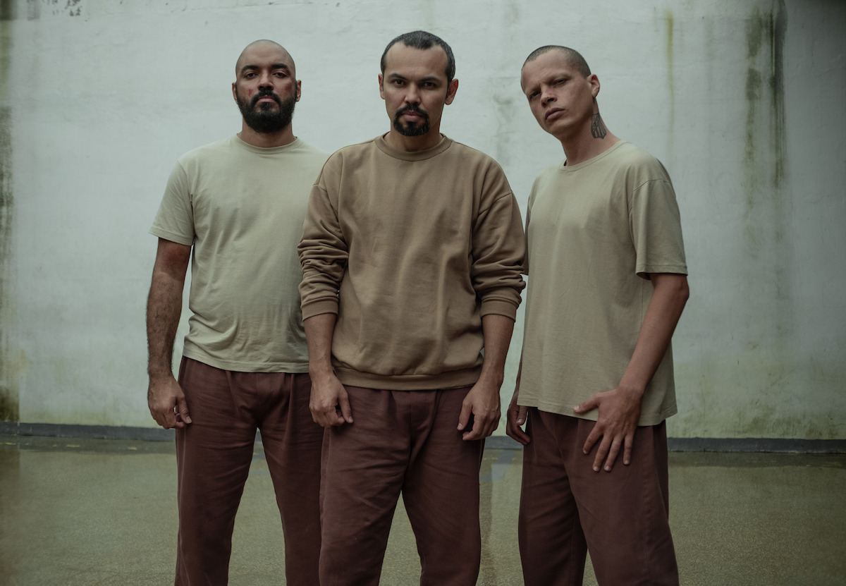 Três homens posam lado a lado em uma penitenciária