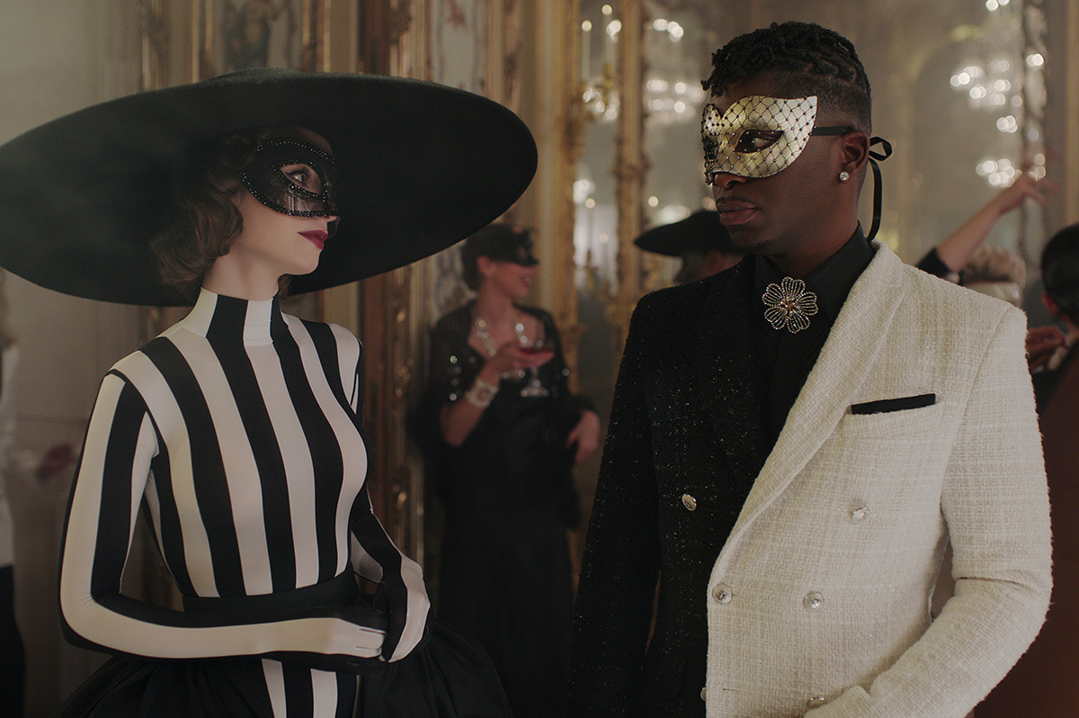 Emily wearing a black and white striped catsuit outfit, paired with a mask and a wide brimmed black hat.