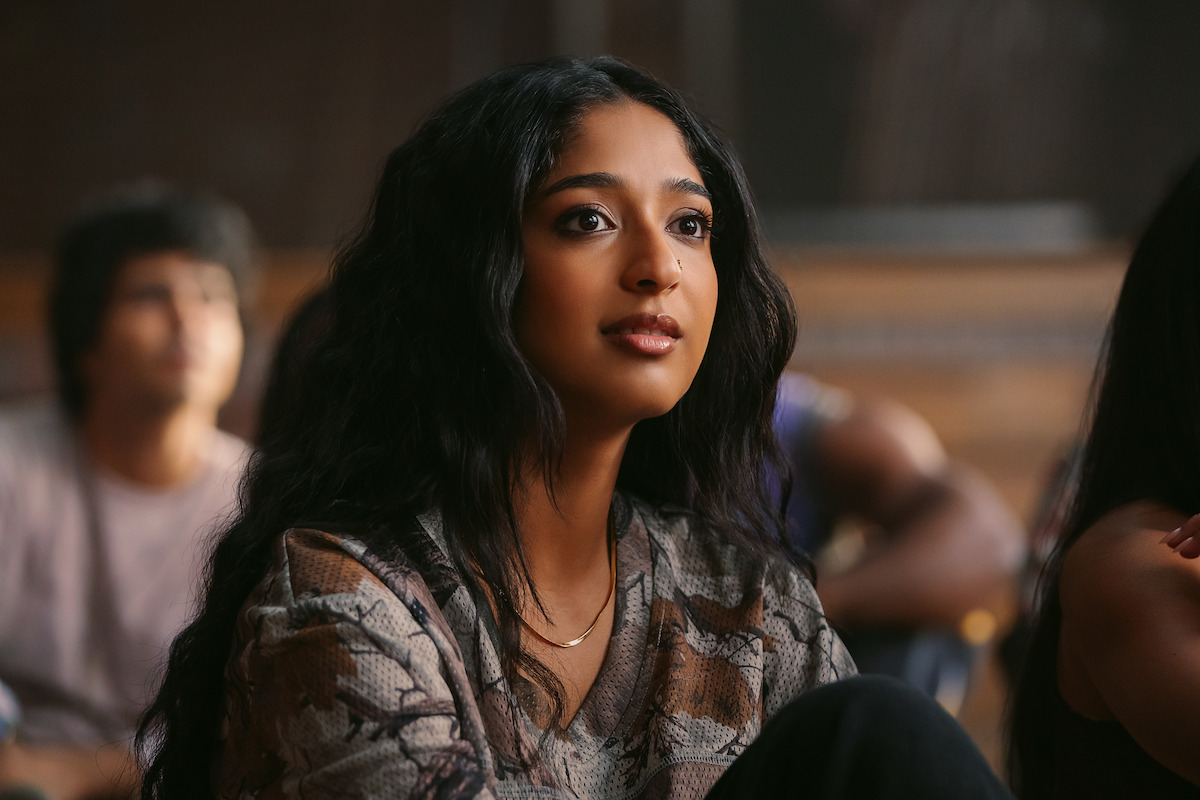 Young woman with long dark hair attentively listening in a classroom setting, softly lit, with other students blurred in the background, creating a focused academic atmosphere.