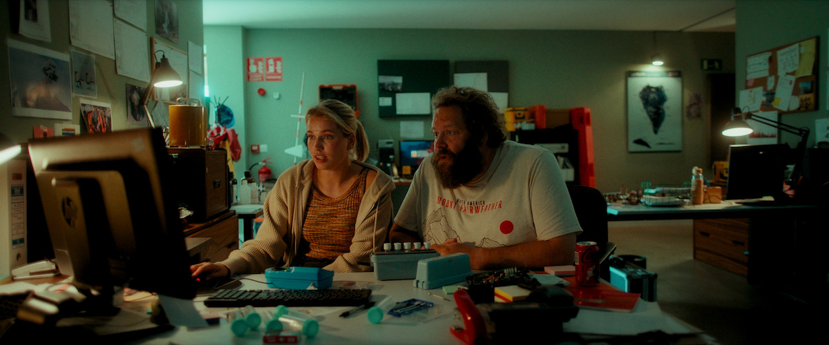 In this image from the series La Palma, Thea-Sophie Loch Ness, who plays Marie Ekdal, and Ólafur Dali Ólafsson, who plays Haukur, sit together by a computer in a dimly lit office.