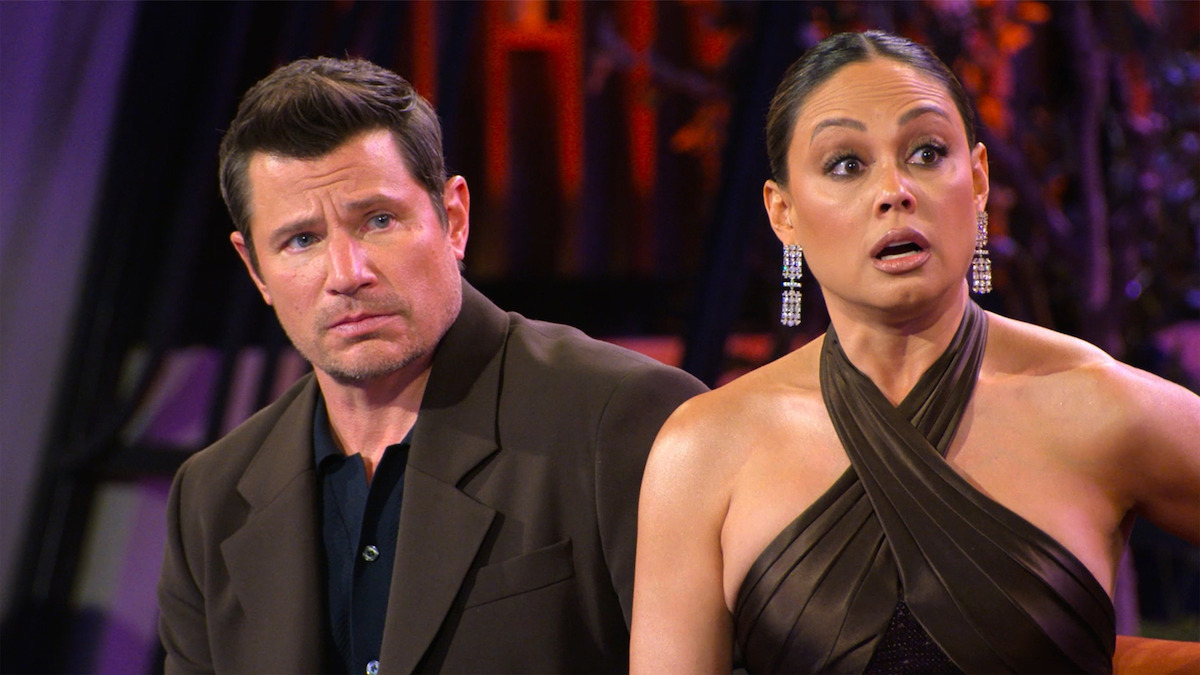 Nick and Vanessa Lachey dressed formally sit indoors, reacting with surprised and serious facial expressions, with colorful lights and abstract decor in the background.