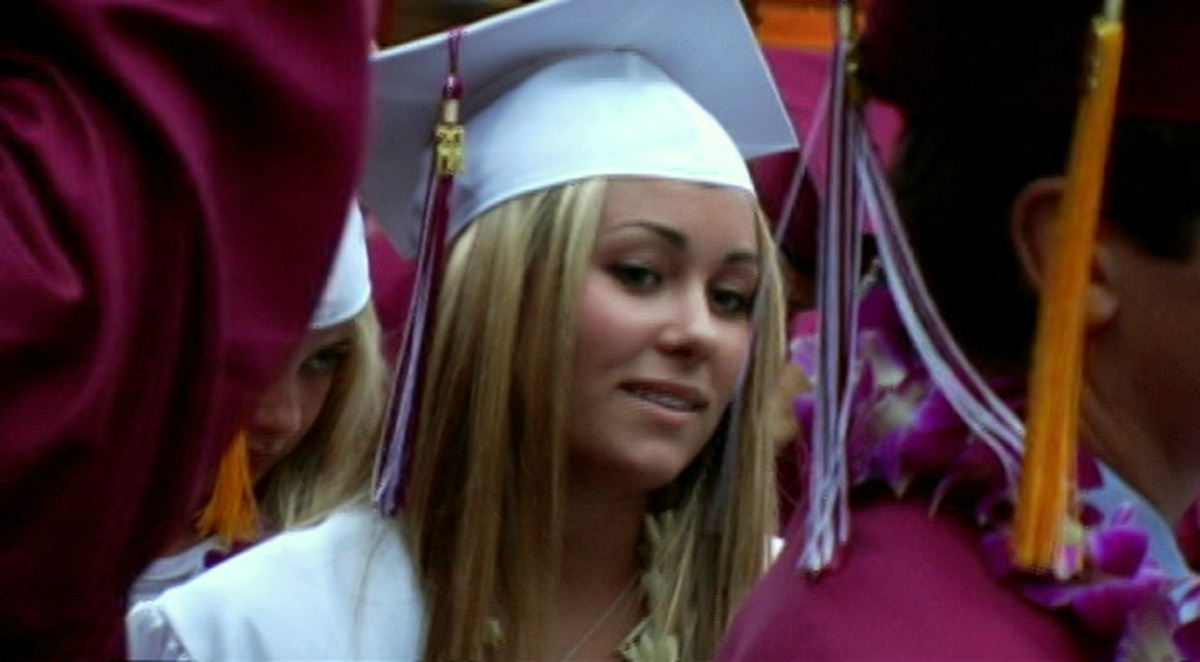 A woman smiling a white graduation cap and robe. 