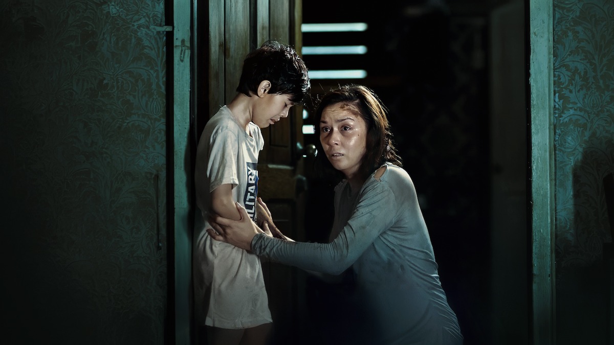 Aiden Tyler Patdu as Lucas cries as Beauty Gonzalez as Iris crouches down to hold his arms as the two stand in a dark hallway, in an image from the film 