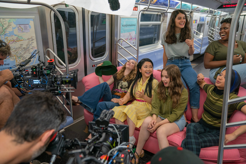 Madeleine Arthur as Christine, Lana Condor as Lara Jean, Emilija Baranac as Gen, and Sofia Black-D'Elia as Heather sitting on a couch in a subway.