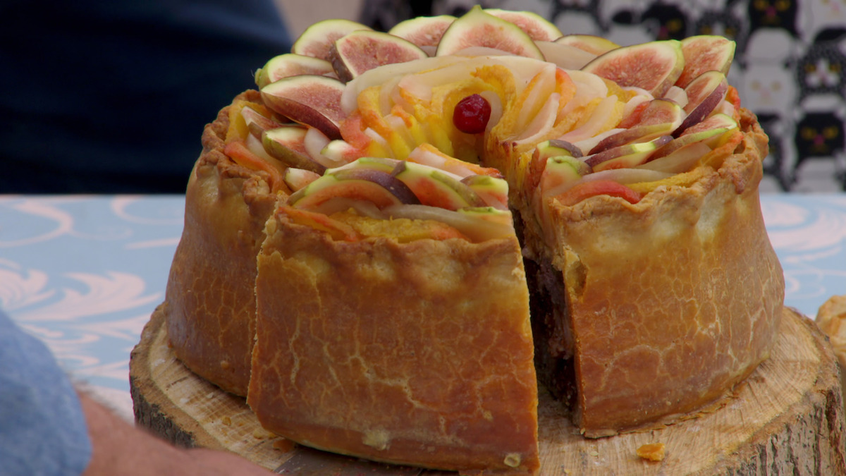 A hand-raised pie that features layers of fruits on top and layers of meats on the inisde
