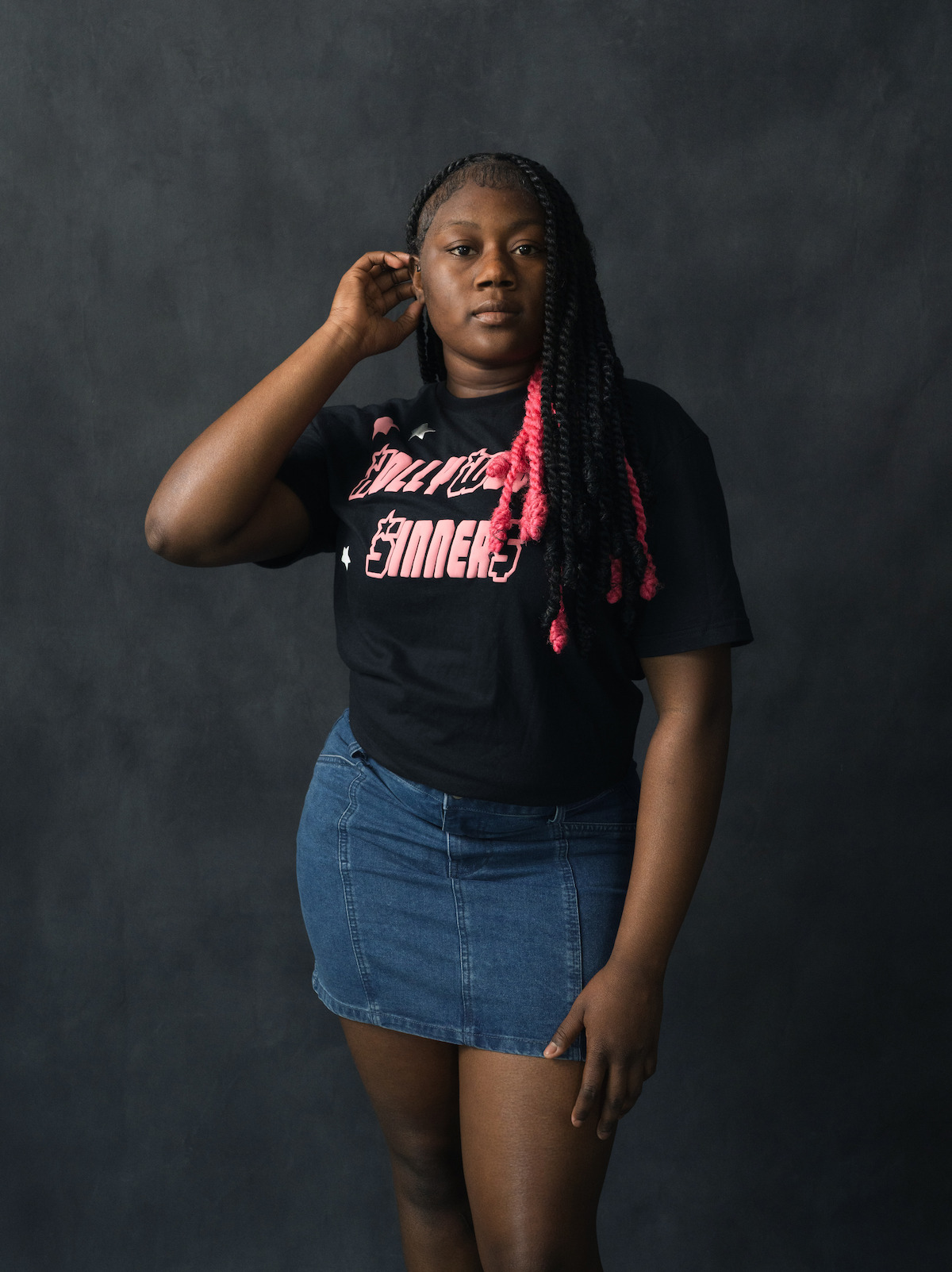 Santana Stewart wears a jean skirt, black shirt, and has pink streaks in her hair.