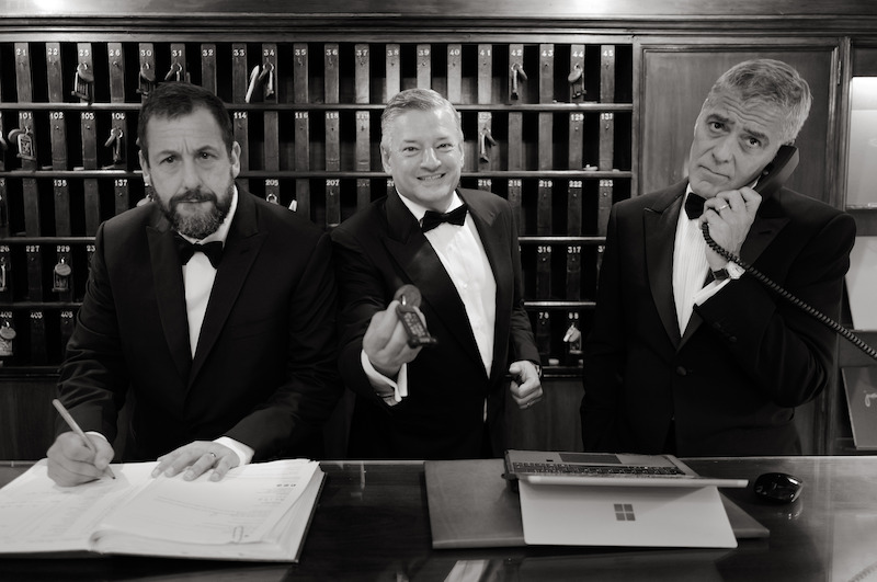 Adam Sandler, Ted Sarandos, and George Clooney pretend to be hotel concierge in tuxedos, with George Clooney answering a phone.