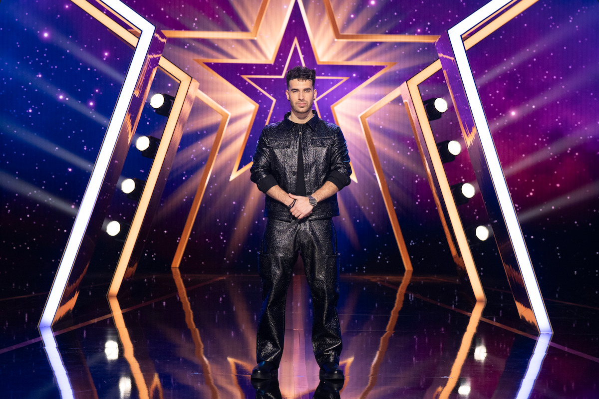 TJ Salta stands center stage with a large illuminated star backdrop and dramatic lighting in a studio set designed for a talent or competition show.
