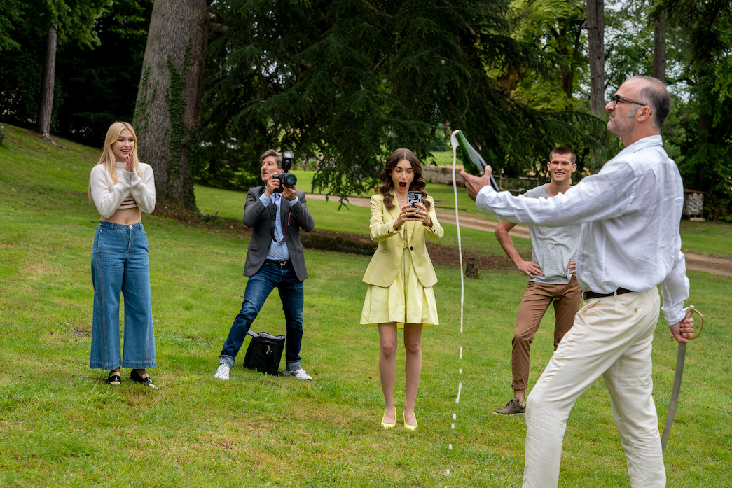 Camille, Emily, and others applaud Camille's father for opening a champagne bottle with a sword