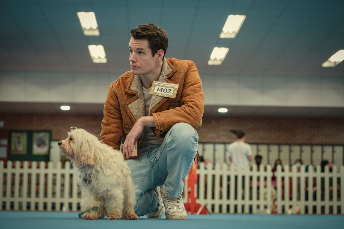 Connor Swindells as Adam Groff kneels and pets his dog at a toy dog agility competition in Season 3 of ‘Sex Education.’