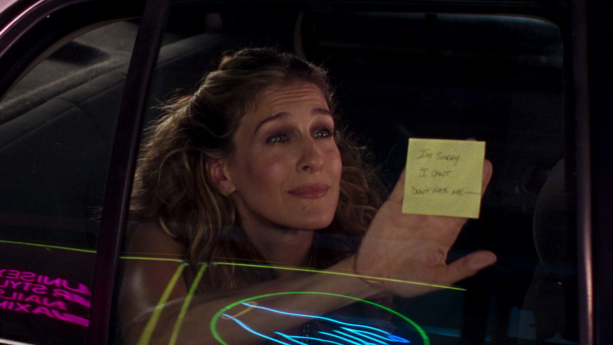 Carrie holding up a post it note against a car window that says 'I'm sorry, I quit Don't hate me -' 