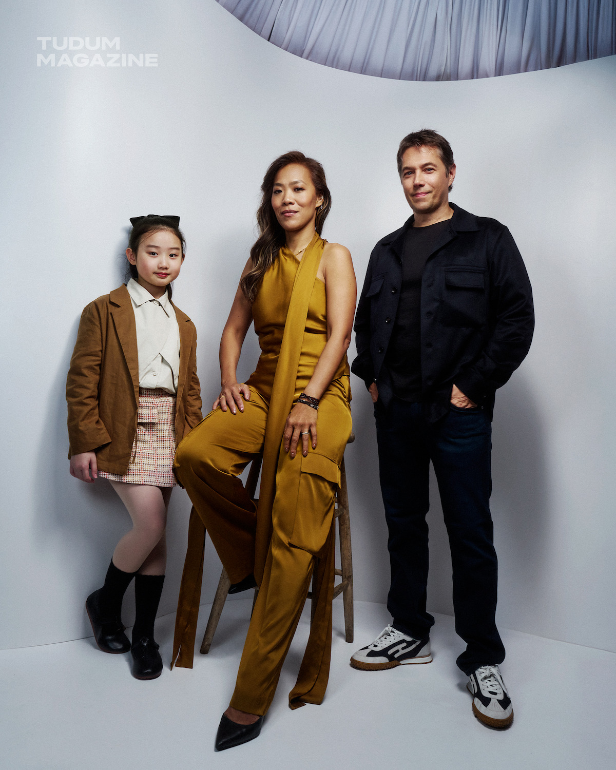 Nina Ye, Shih-Ching Tsou, and Sean Baker stand against a white backdrop, with Shih-Ching Tsou sitting on a stool in the middle.
