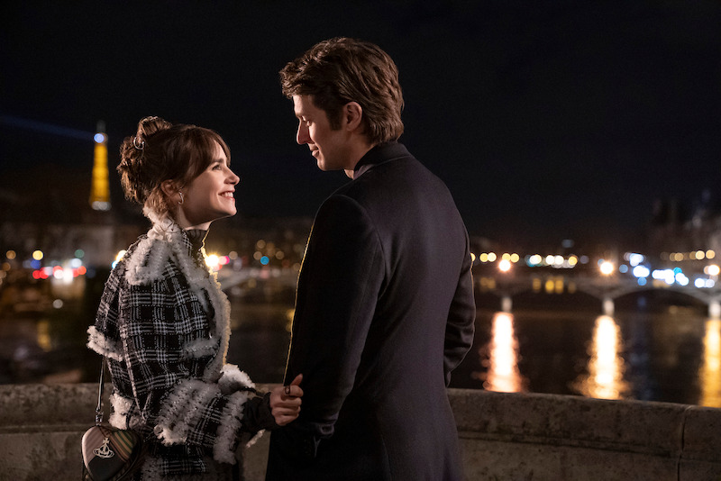 Lily Collins as Emily and Lucas Bravo as Gabriel smile at each other on a bridge in Season 4 of 'Emily in Paris'