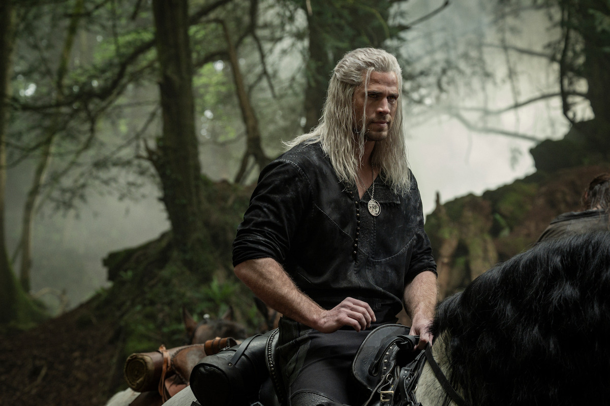 A man with long white hair in medieval clothes rides a horse through a misty, dense forest. The setting feels mysterious, tense, and adventurous.