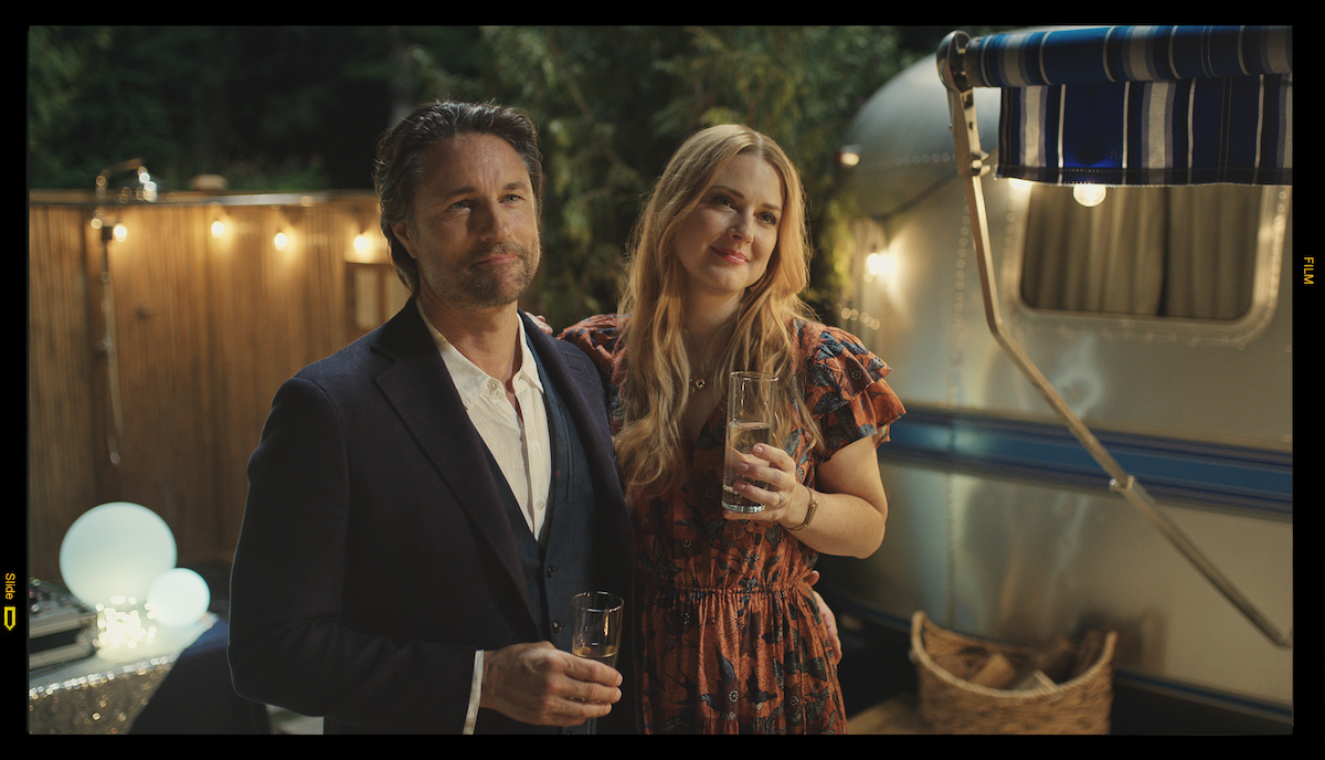 Martin Henderson as Jack Sheridan and Alexandra Breckenridge as Mel Monroe smile together at an outdoor party in ‘Virgin River.’