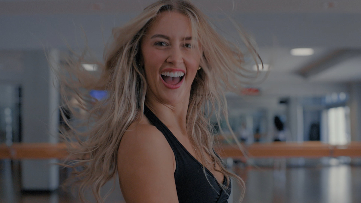 Smiling woman with long blonde hair dancing in a bright fitness studio, wearing athletic clothing, with mirrored walls and wooden ballet barres in the background.Smiling woman with long blonde hair dancing in a bright fitness studio, wearing athletic clothing, with mirrored walls and wooden ballet barres in the background.
