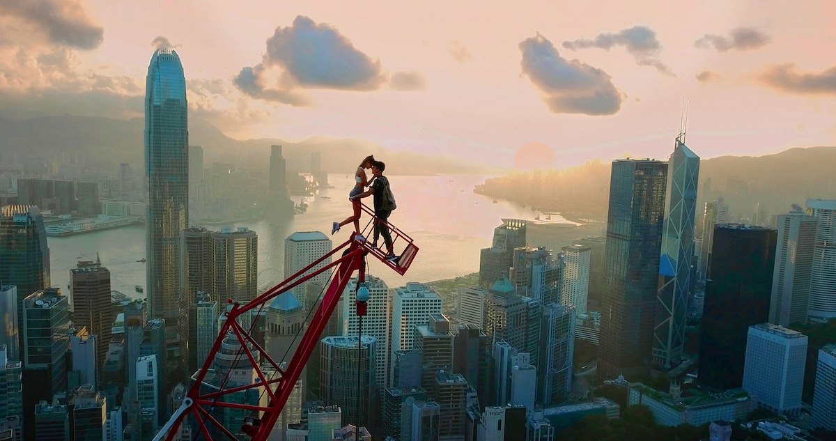 Two people standing on top of a high rise crane, overlooking a beautiful city-scape. 
