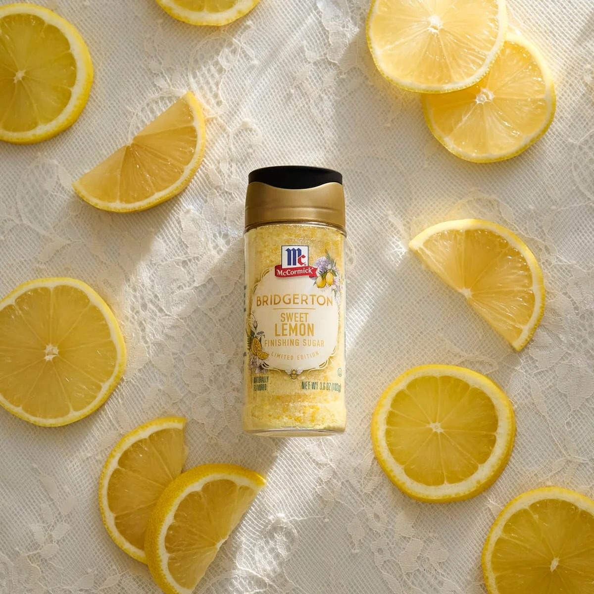 McCormick Bridgerton Sweet Lemon seasoning bottle on white lace fabric, surrounded by sliced lemons in sunlight.