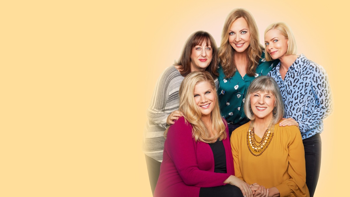 Five women posing together and smiling in front of a light yellow background. They are dressed in casual to semi-formal clothing, suggesting a friendly and supportive environment, possibly a promotional image for a TV show or group.