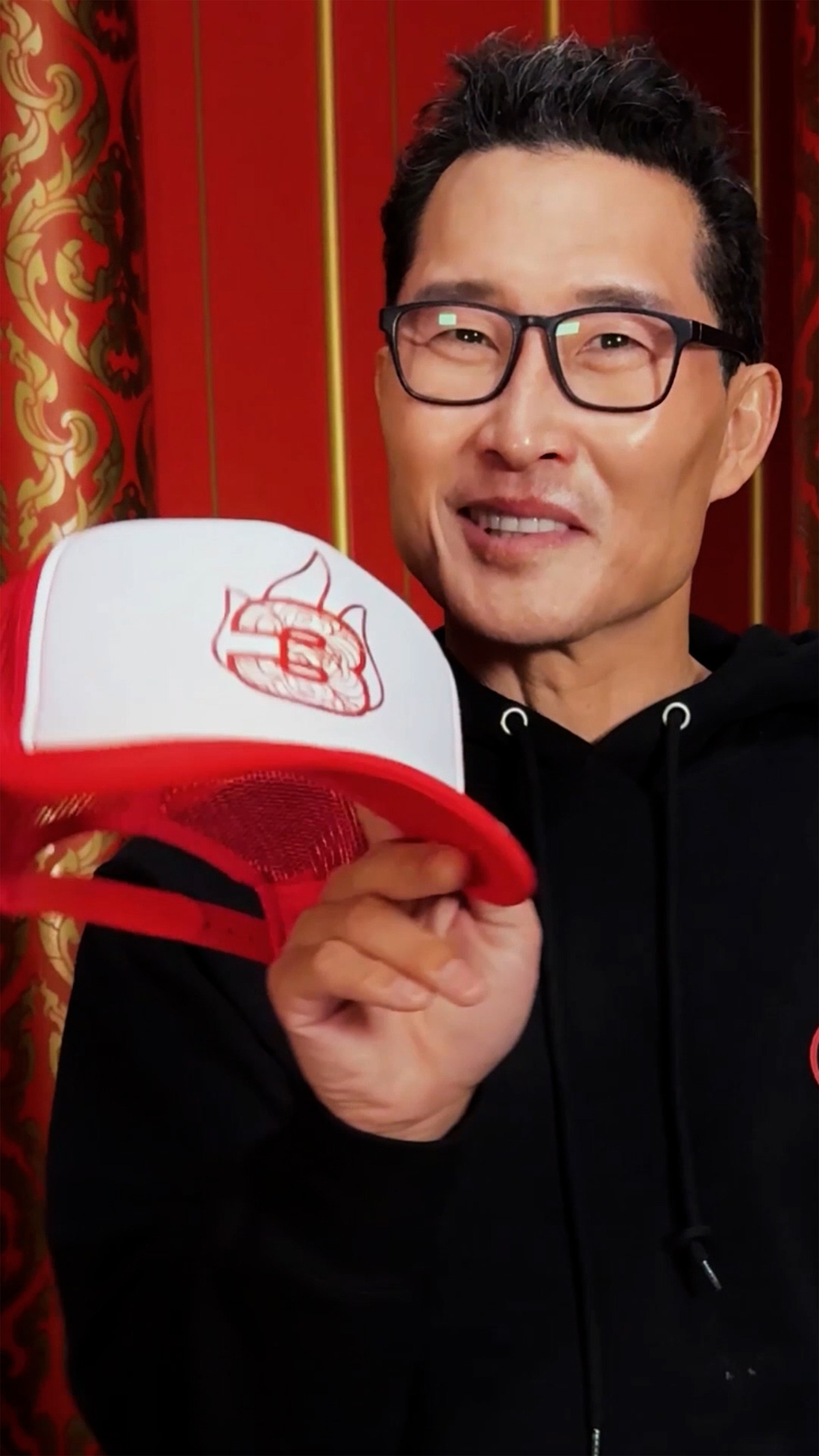 Daniel Dae Kim holds a hat with a 3 and the 'Avatar: The Last Airbender' Fire Nation logo on it. 