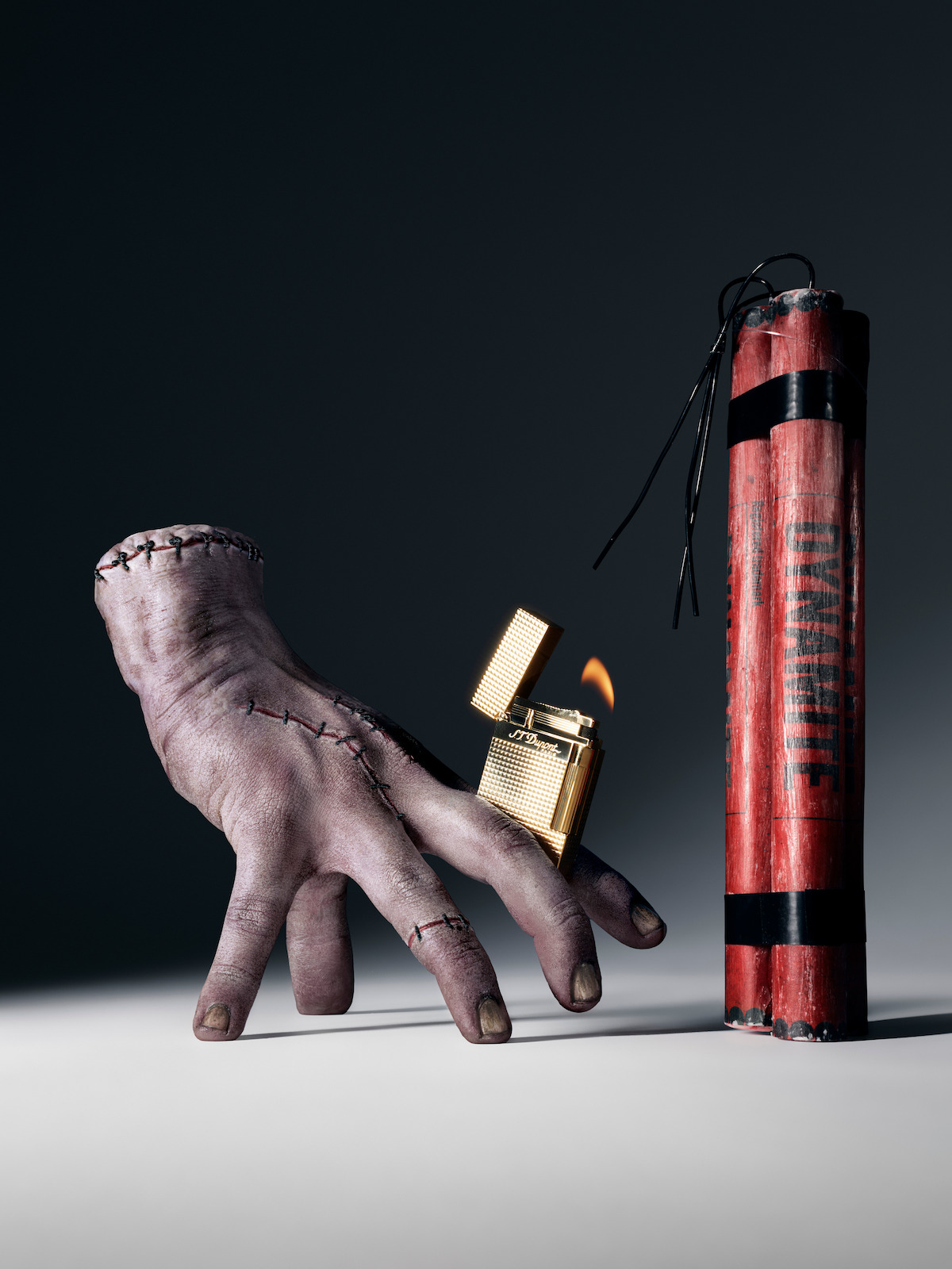 Thing holding a lit lighter next to sticks of dynamite.