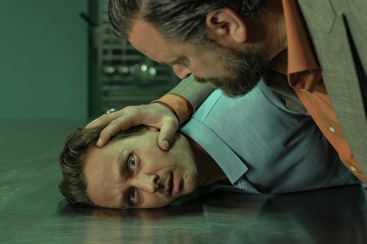 Sascha Geršak presses Tom Schilling's head with his hand onto a steel surface in an image from 