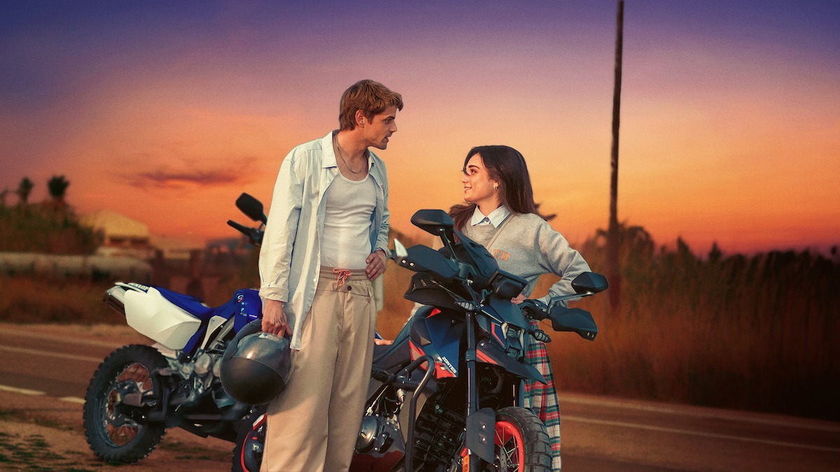 Alberto Olmo as Eros Douglas and Eléa Rochera as Reese Russell stand beside two motorbikes during sunset on the side of a road in an image from ‘Bad Influence.’