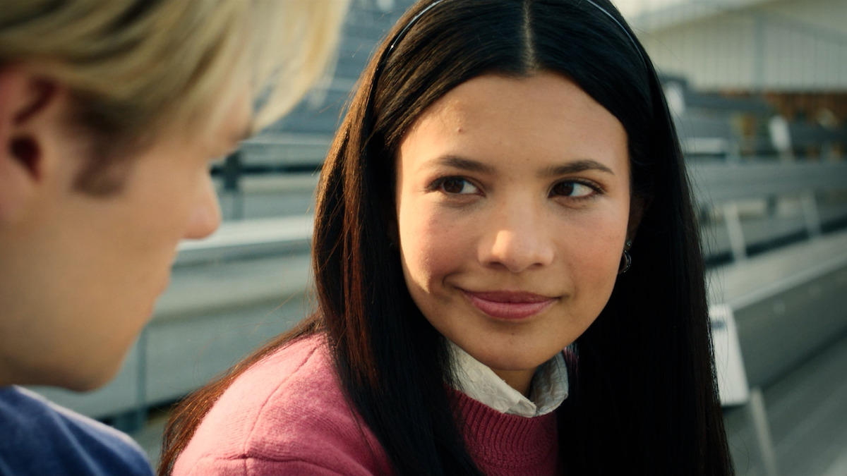 A young girl in a pink sweater smiles at a blond boy.