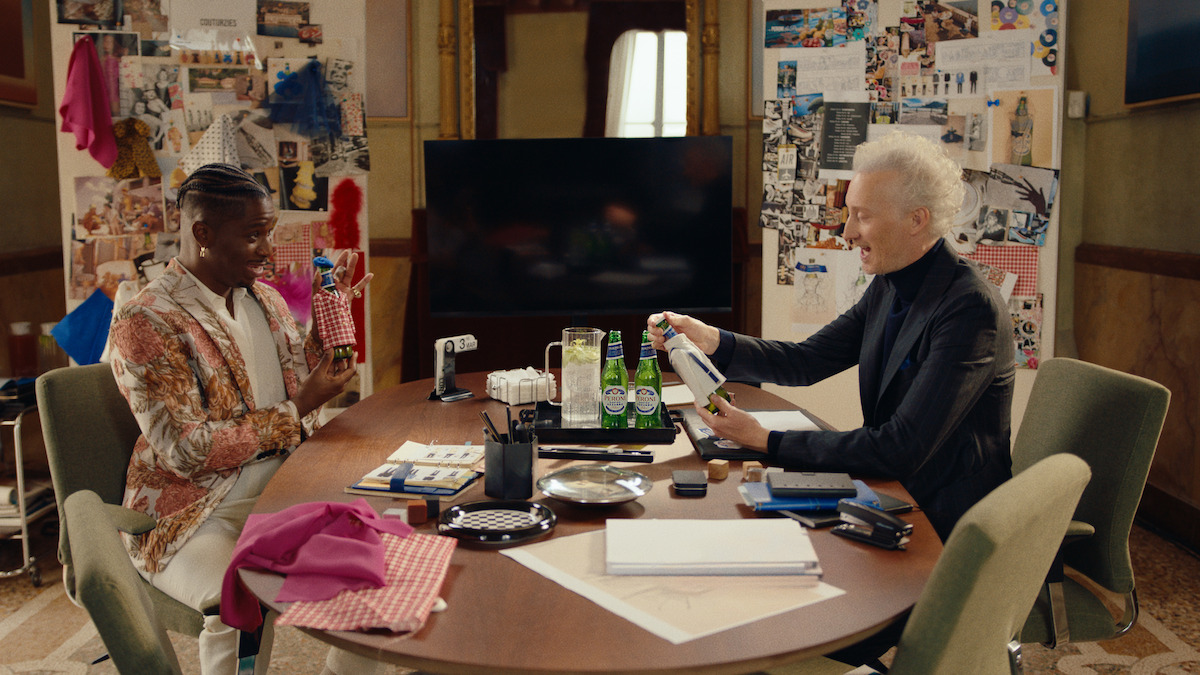 Bruno Gouery as Luc and Samuel Arnold as Julien sit at a round table in a collage-filled office.