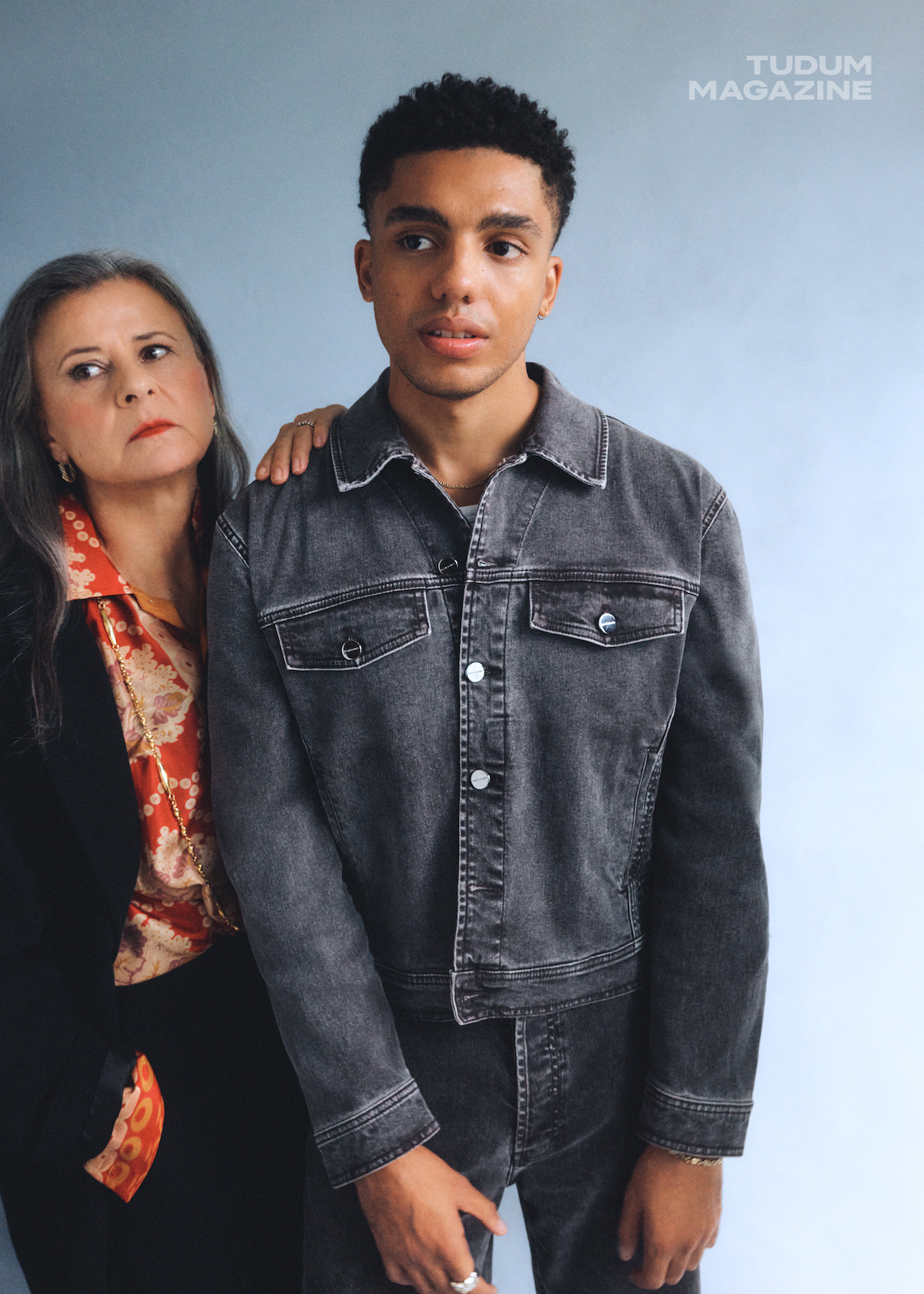 From left to right, Tracey Ullman and Jay Lycurgo pose together against a blue wall.