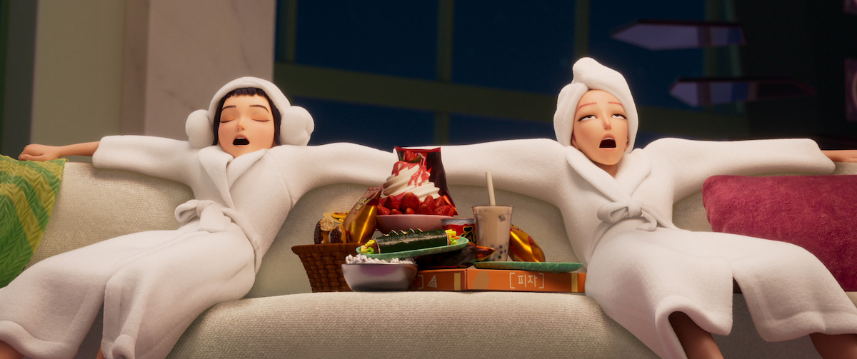 Zoey and Mira sit on a couch with food in ‘KPop Demon Hunters’