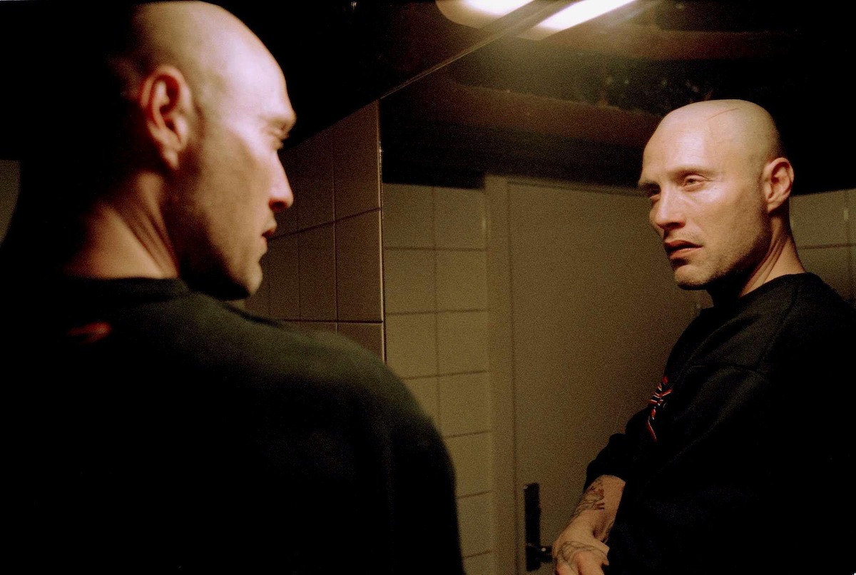 Tonny (Mads Mikkelsen) looks at himself in the mirror, wearing a dark sweatershirt.