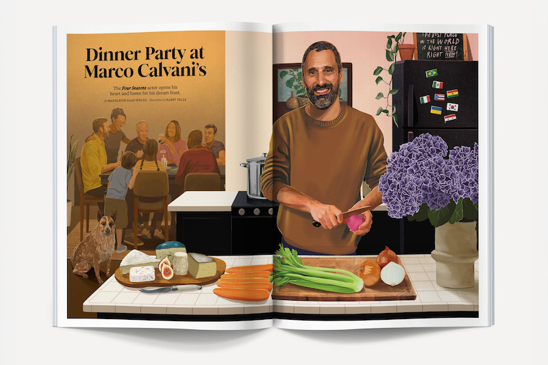 Man prepares food in a kitchen with vegetables, cheese, and flowers on the counter; behind him a group of people sit around a dinner table; a dog sits on the floor; stylish modern setting with art and plants.