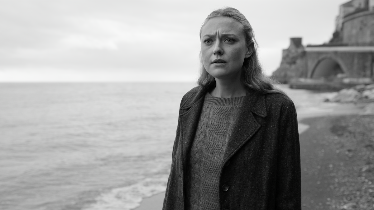 Black-and-white photo of Dakota Fanning and Marge standing on a beach with a concerned expression in ‘Ripley’