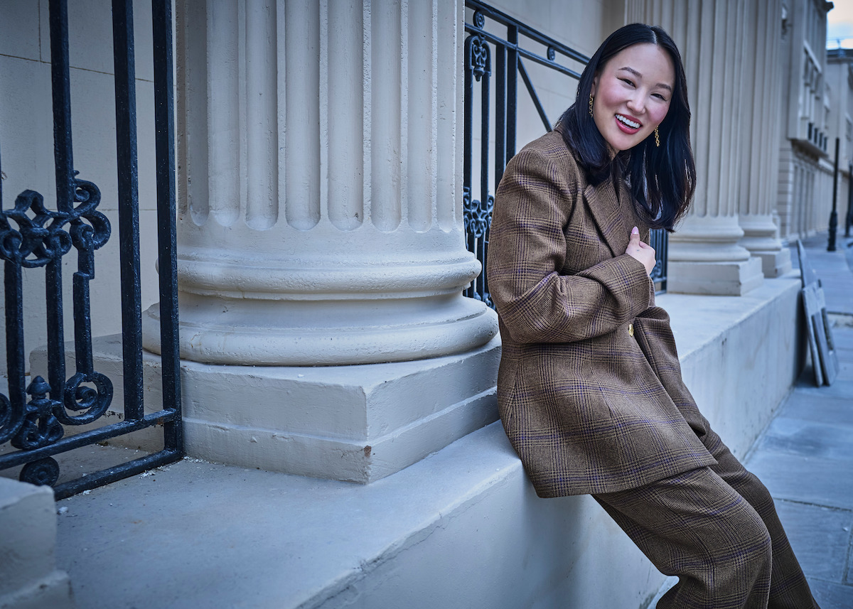Yerin Ha wears a brown suit and leans on a large pillar.